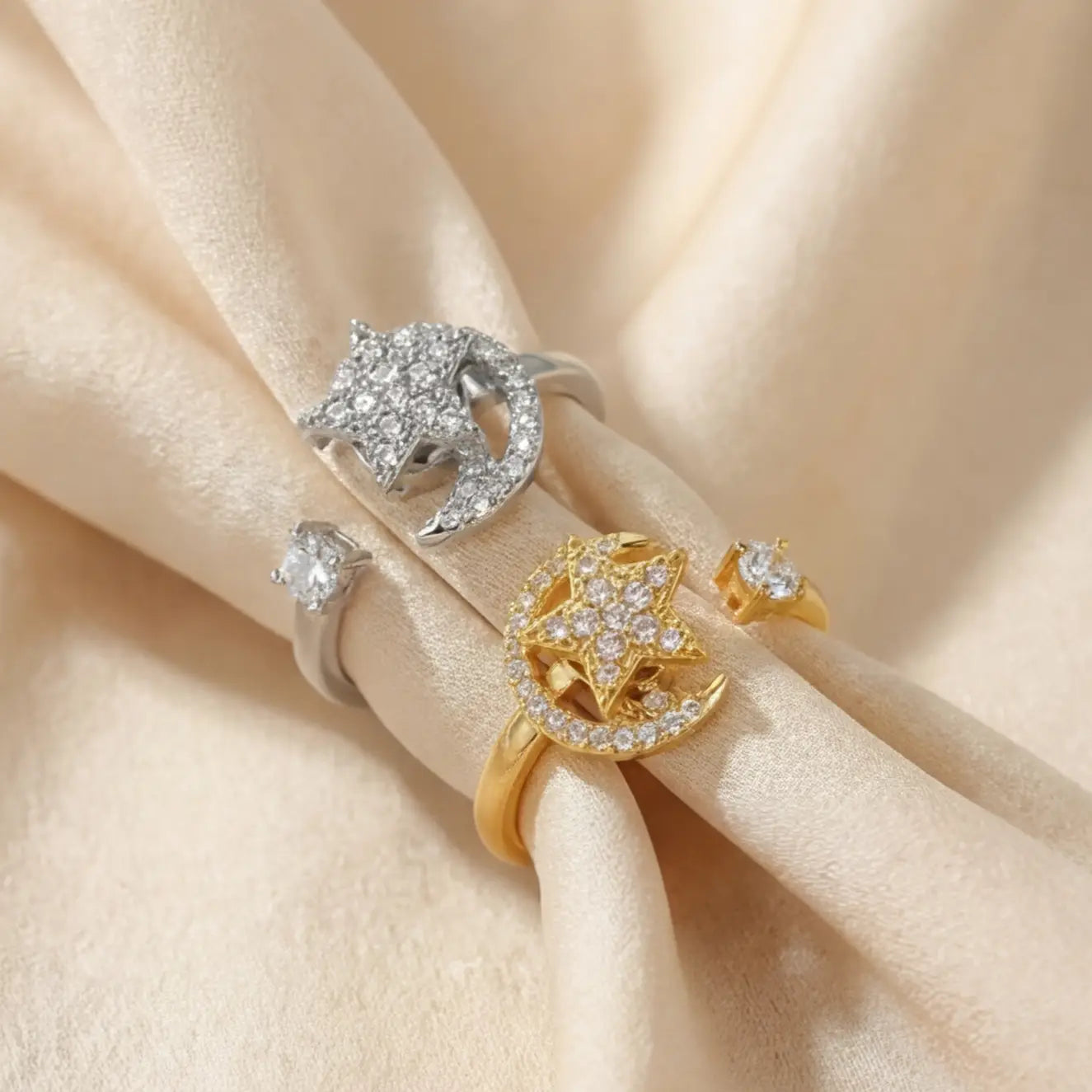 A pair of gold and silver Pausa spinning sun star fidget calm rings resting on champagne silk folds.