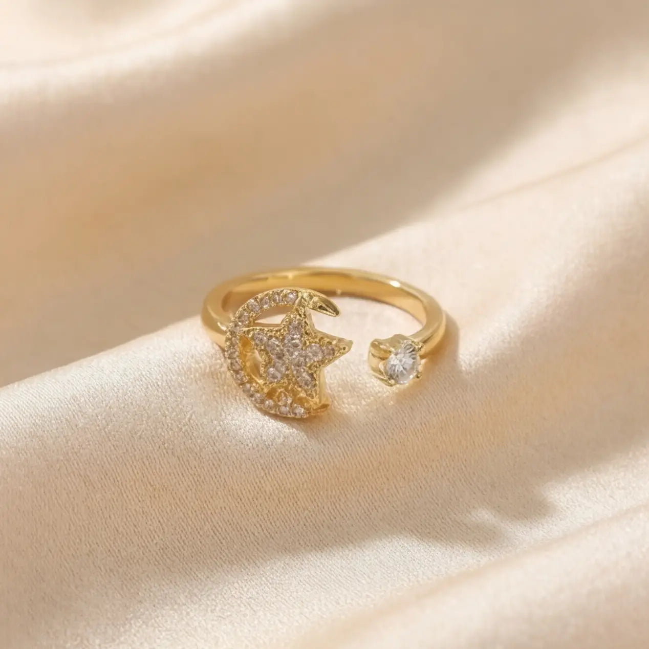 Styled wide-angle shot of a gold Calm spinning sun open ring on draped silk material.