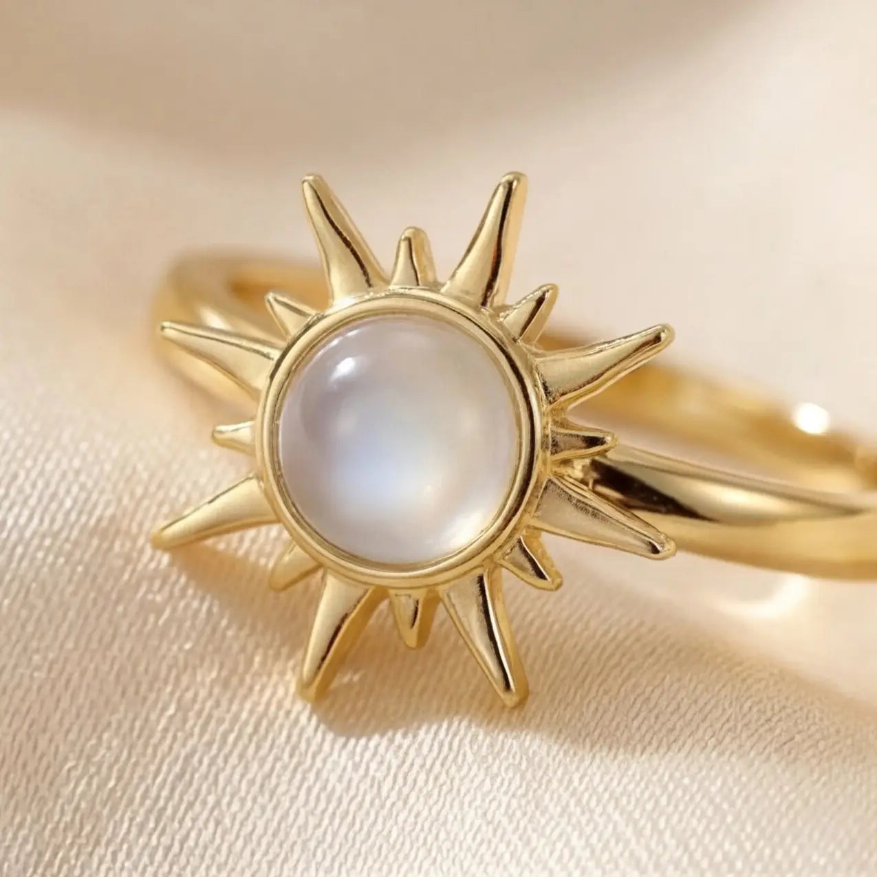 Gold sunburst calm ring with round moonstone center on soft fabric background