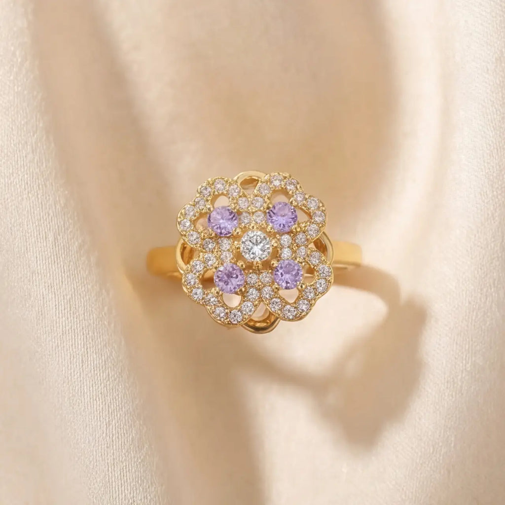 Gold clover flower calm ring with purple and clear stones on cream fabric