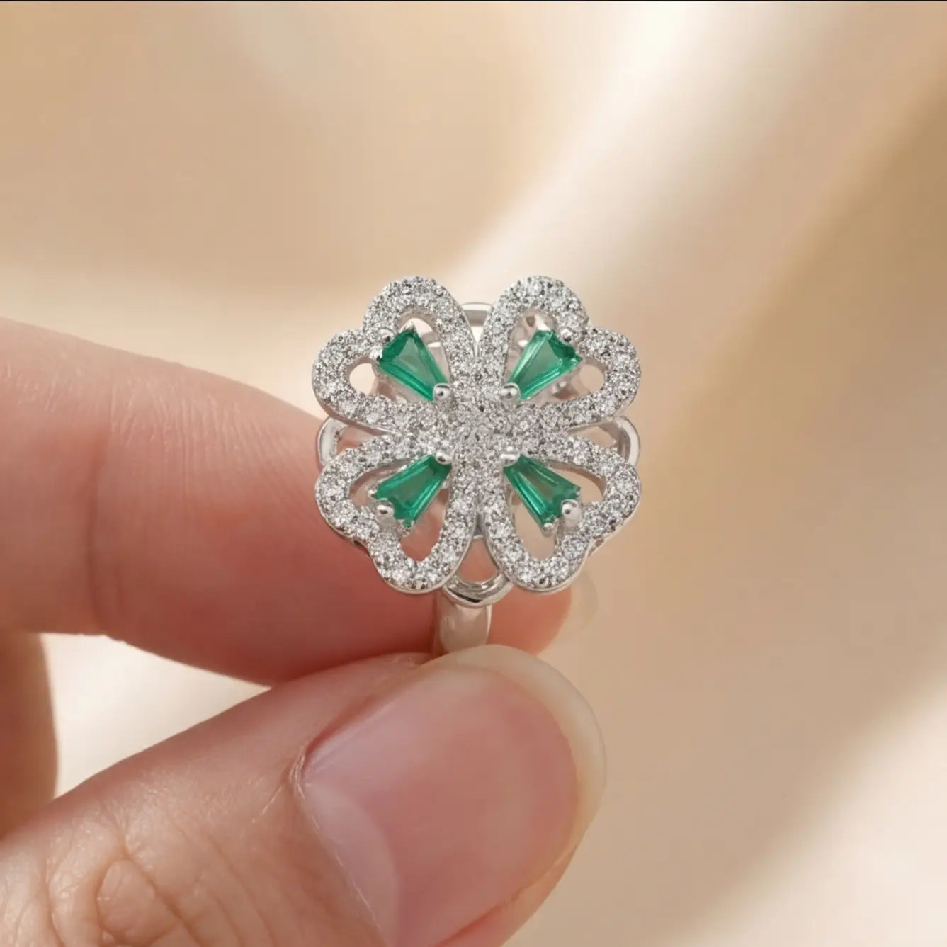 Silver clover flower calm ring with green stones held between fingers for size reference