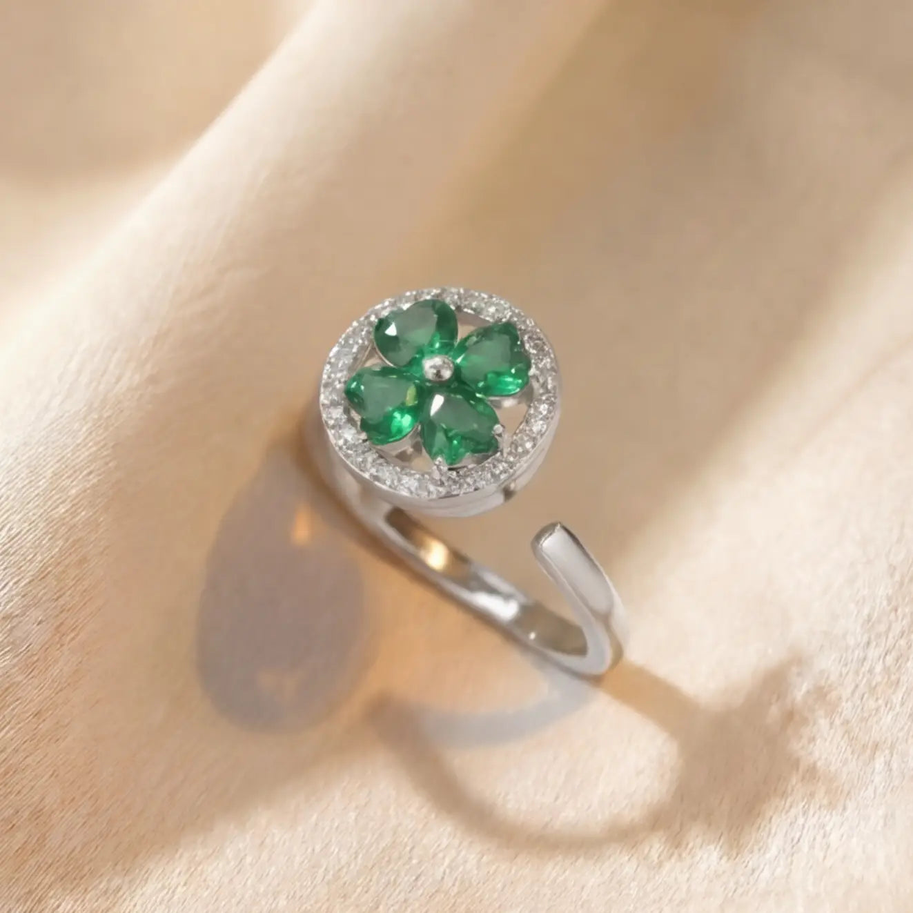 Lunela Metà silver calm spinner ring with green heart cut clover stones and pavé halo on champagne satin