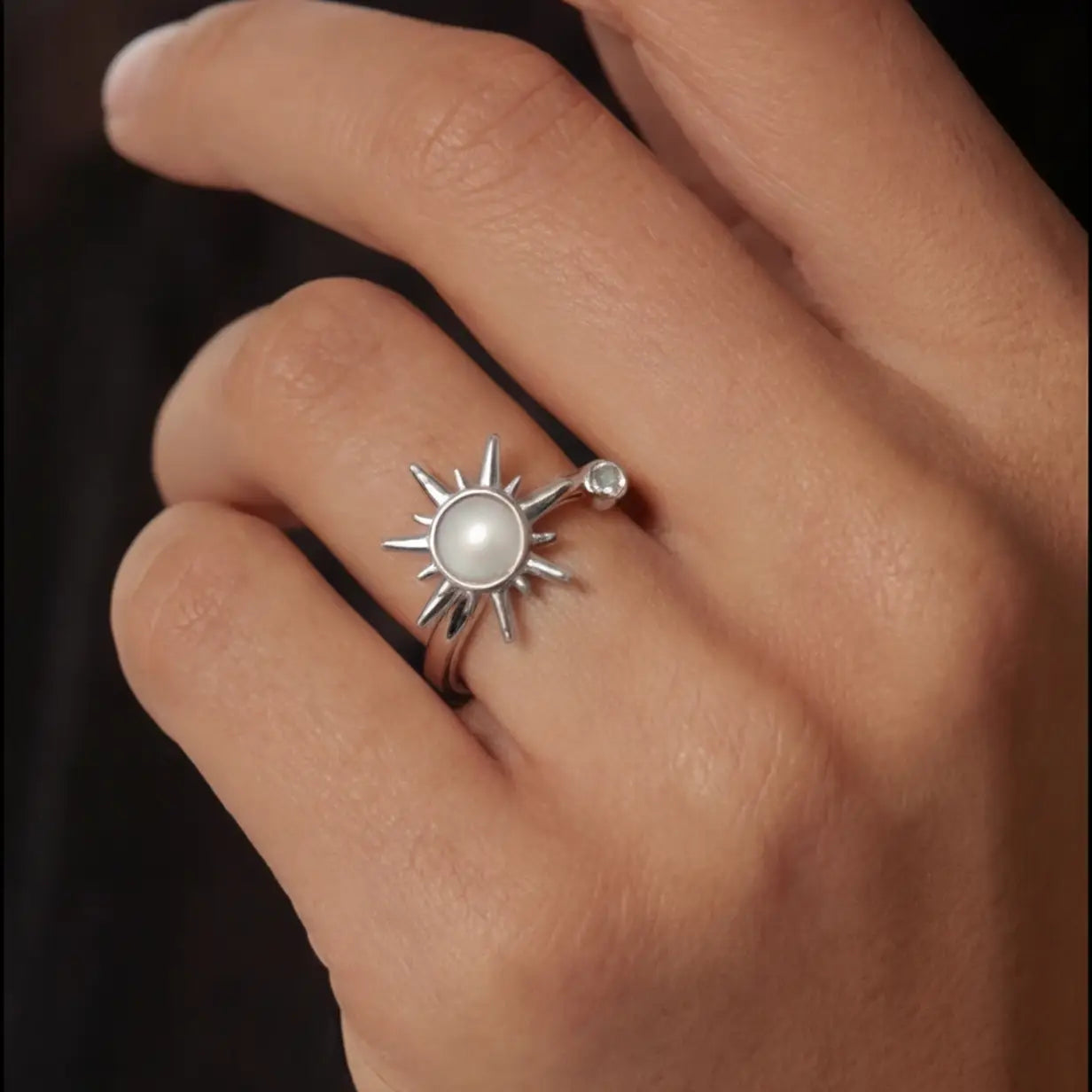 Silver Raggio sunburst calm ring with moonstone center worn on hand against dark background